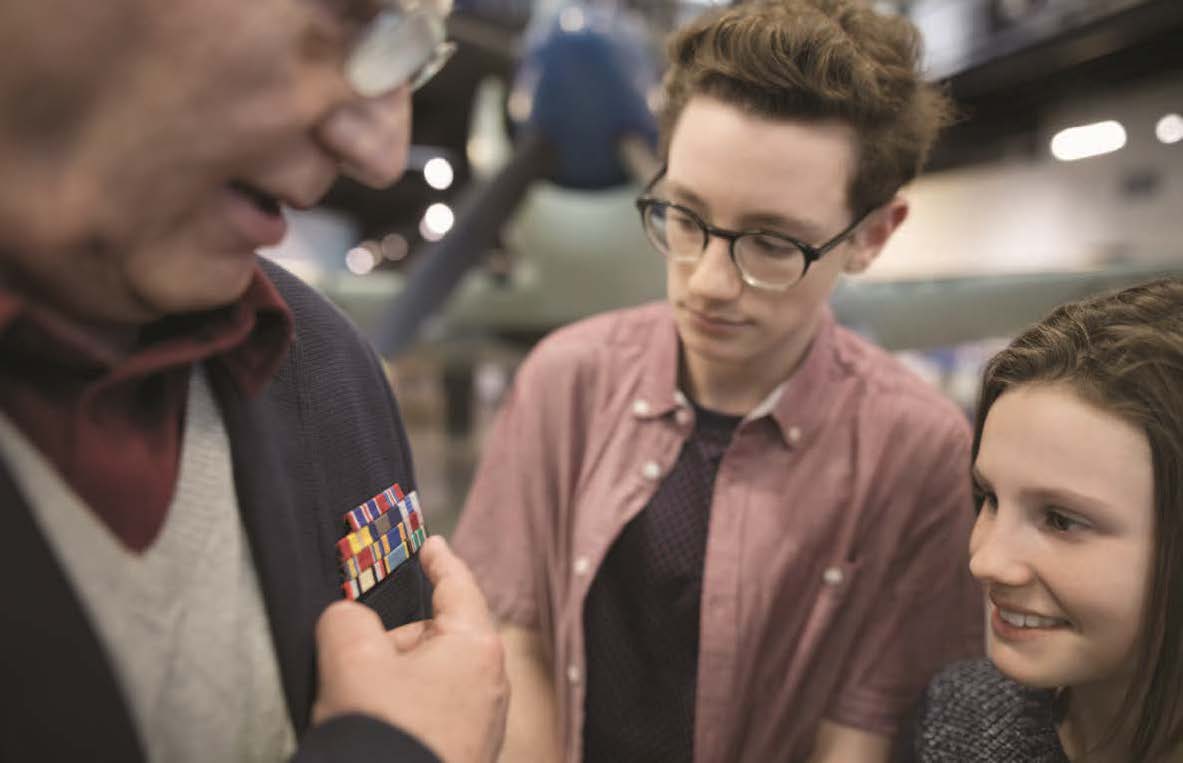 Two young people examine an elderly man's military decorations.