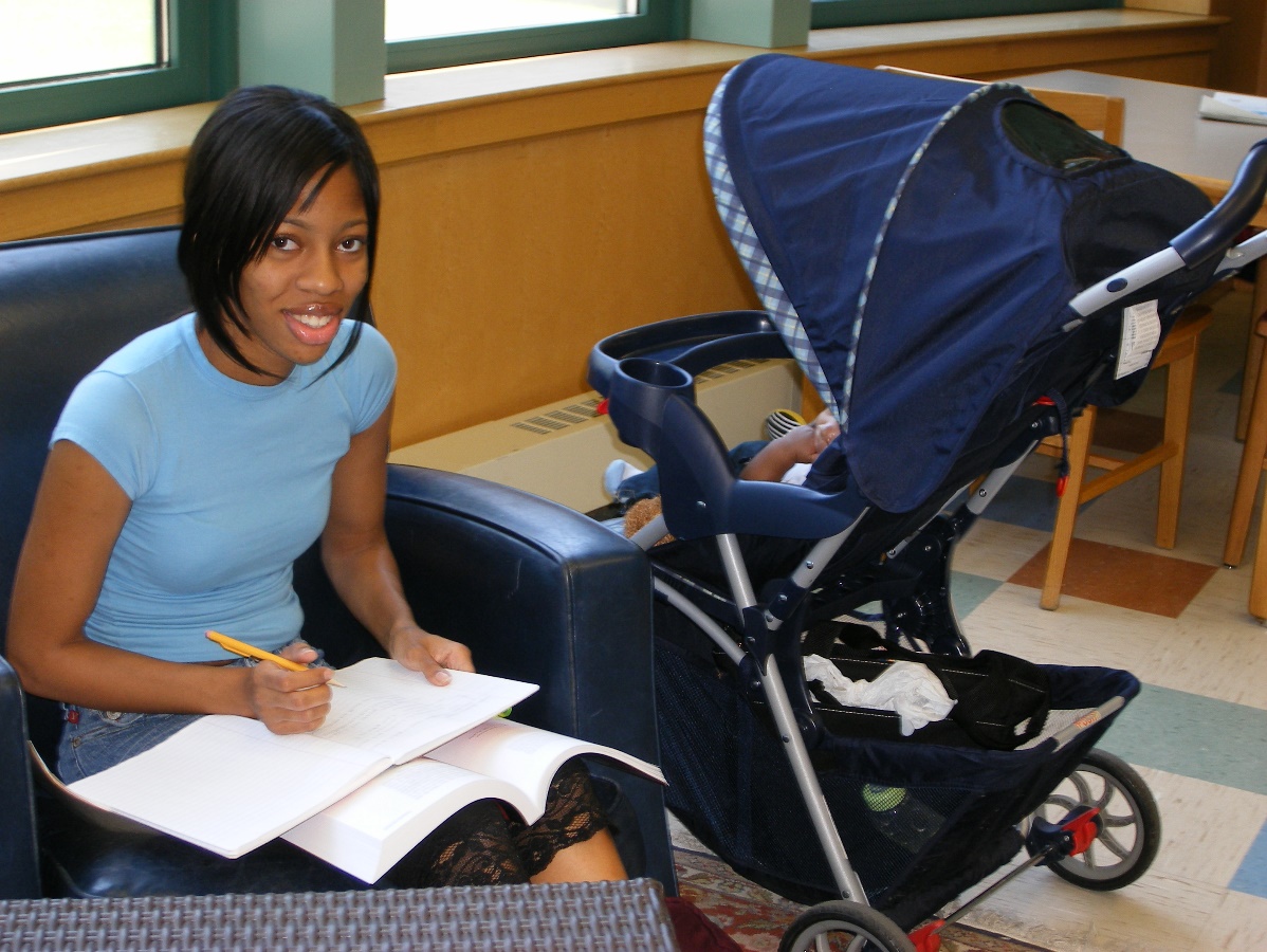 A woman writing and sitting next to a stroller.
