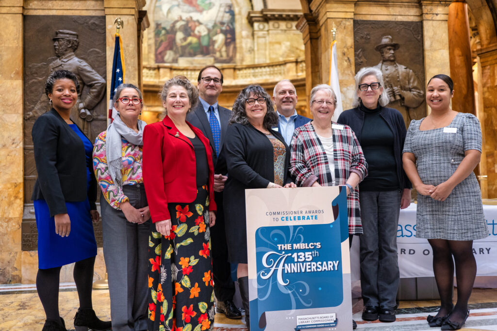 Group photo of the MBLC Commissioners at the Commissioner Awards on November 6, 2025, at the Massachusetts State House, posing behind a sign that reads “The MBLC’s 135th Anniversary,” with historic statues and murals visible in the background.