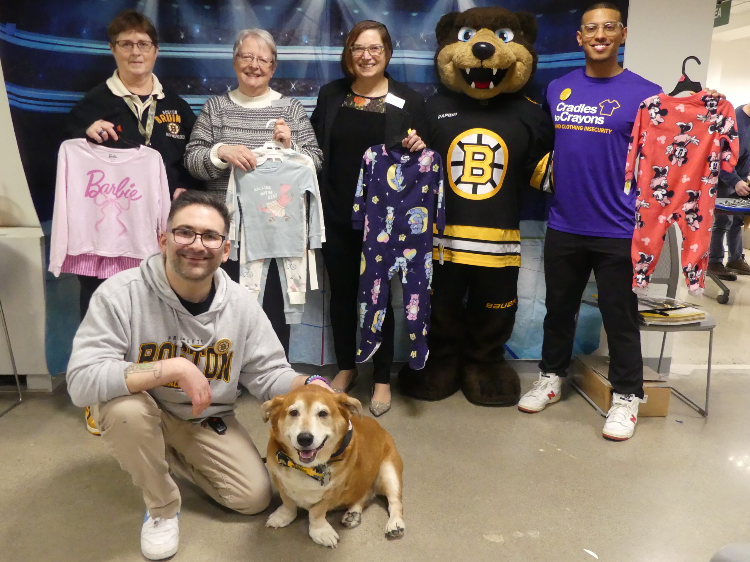 Staff from Bridgwater Public Library pose with Ollie, the service dog, MBLC Director Maureen Amyot, Commissioner Debby Conrad, and representative from Cradles to Crayons at a Bruins PJ event.
